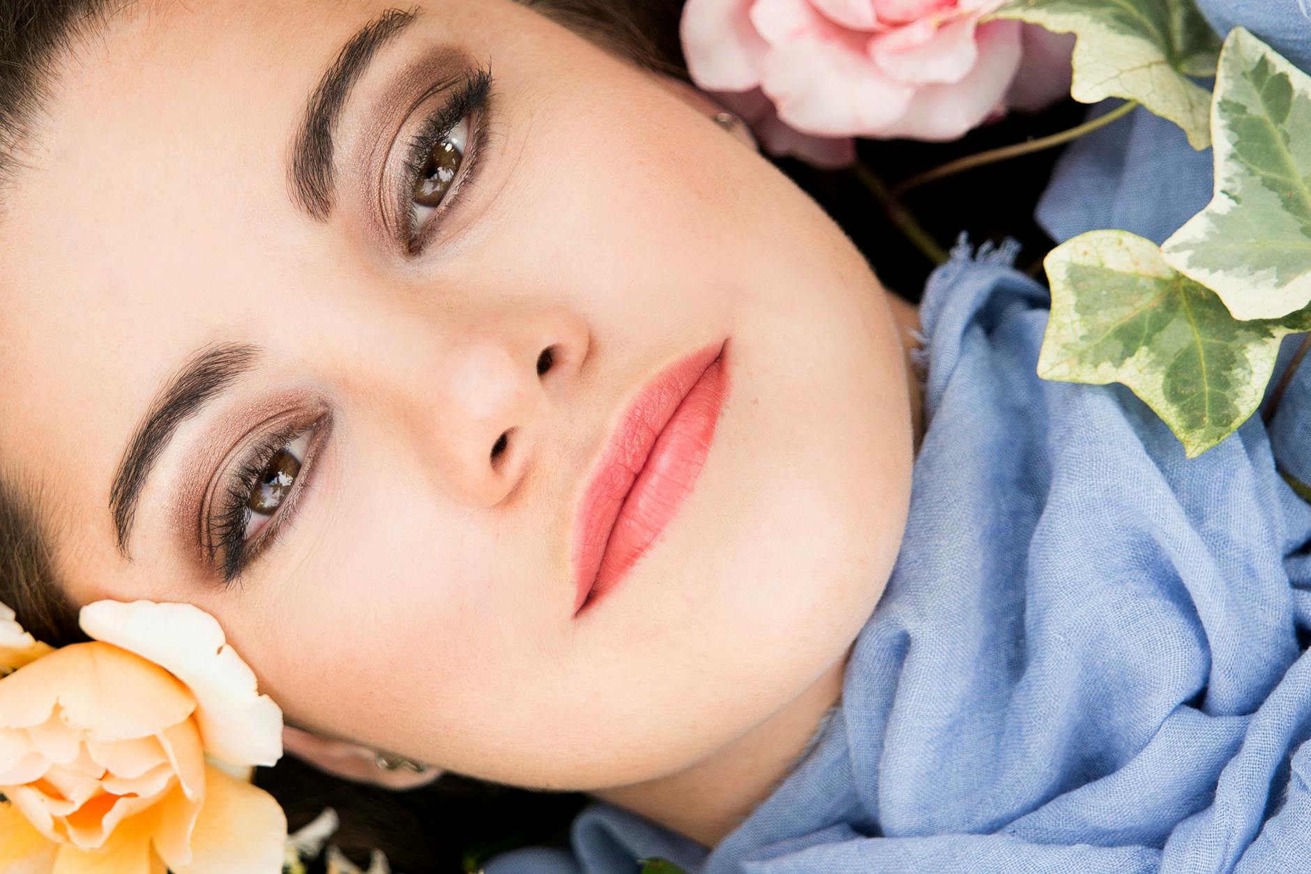 Zbliżenie młodej kobiety w naturalnym makijażu wśród różowych i żółtych kwiatów