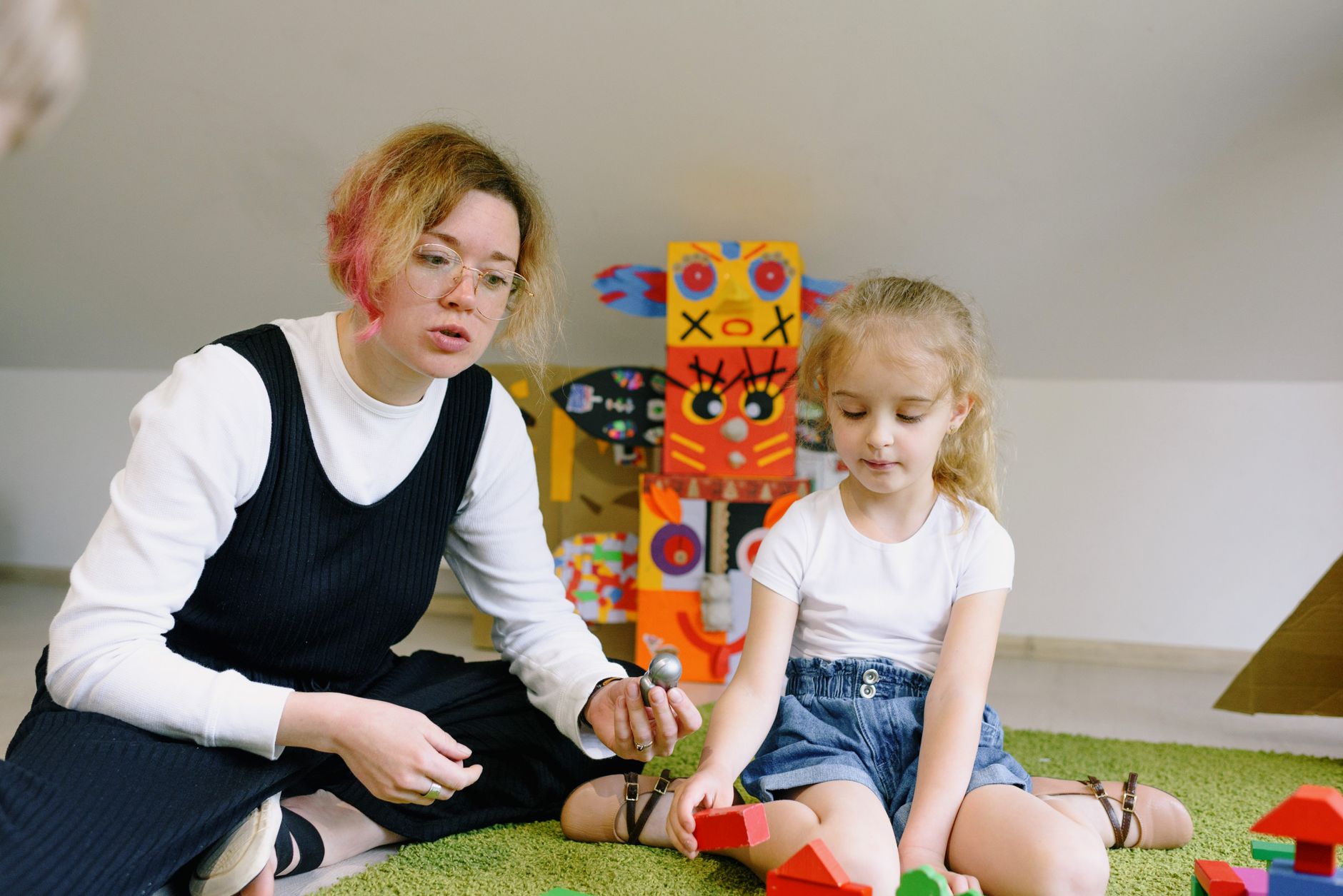 Jak wspierać adaptację dziecka w przedszkolu dzięki prostym rytuałom i spokojnej komunikacji z nauczycielami Mama i dziecko bawią się kolorowymi klockami w przedszkolnej sali