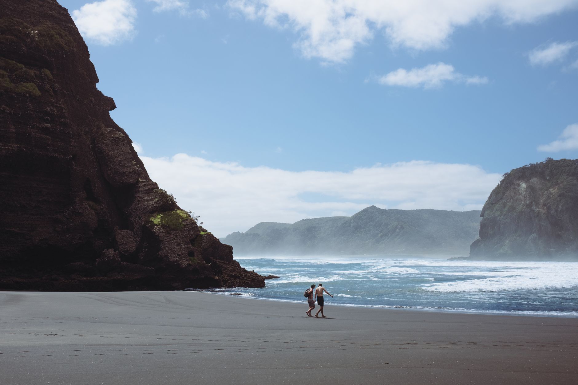 Plaża Piha koło Auckland, fale oceanu i dwie osoby spacerujące brzegiem